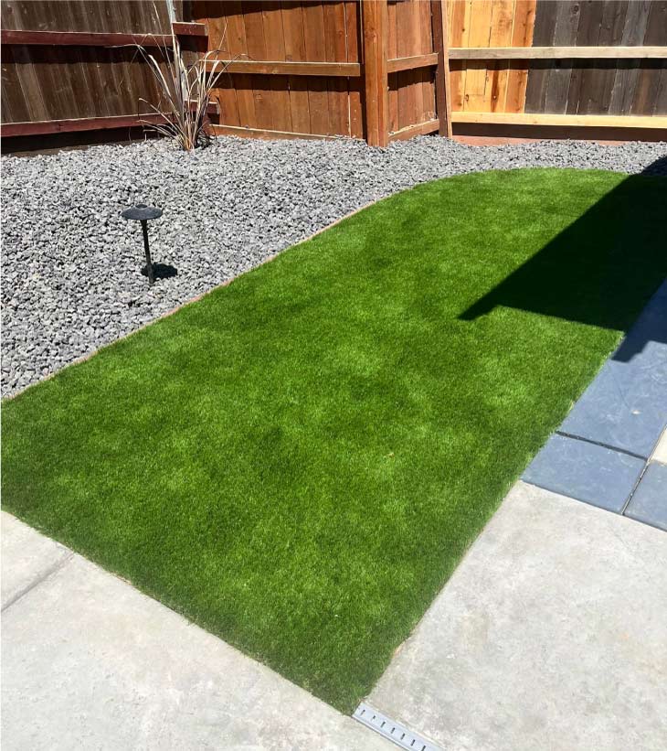 High-efficiency backyard irrigation installation featuring a small patch of vibrant sod bordered by dark river rock and professional landscape lighting.