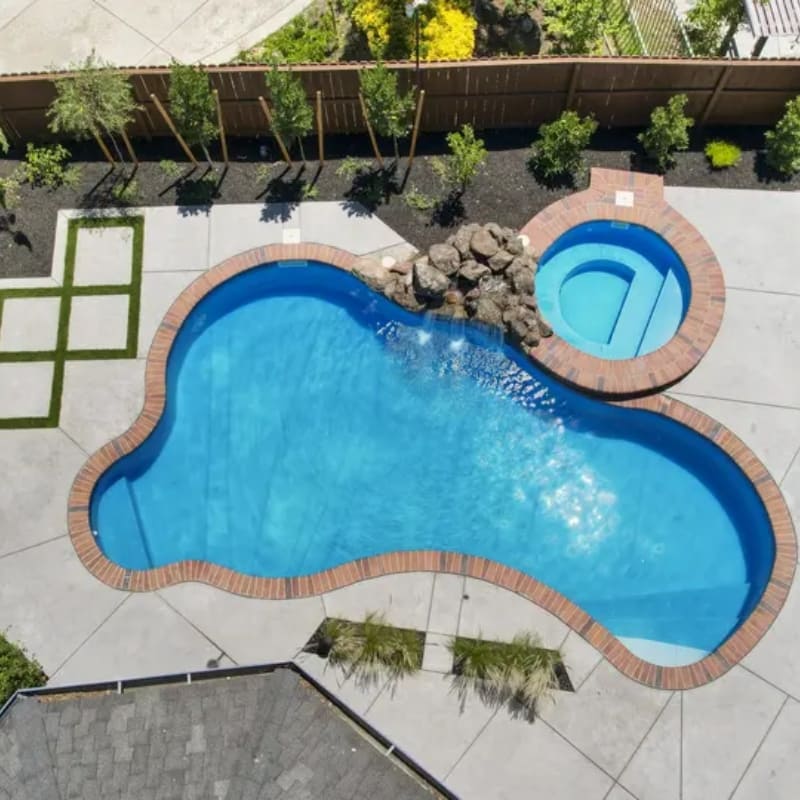 Luxury backyard pool design in El Dorado Hills featuring a custom rock waterfall, integrated spa, and a modern stamped concrete deck with artificial turf accents.