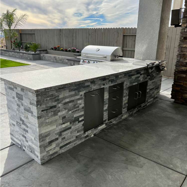 Complete outdoor living transformation with a modern stone-finished kitchen island, integrated storage drawers, and high-performance grilling equipment.