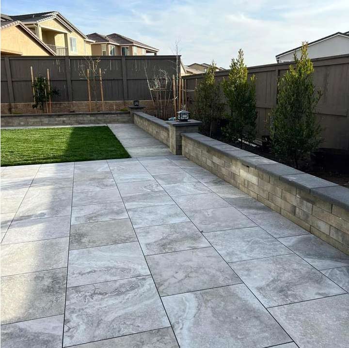 Modern grey square patio pavers installed with a stacked stone retaining wall and manicured lawn for low-maintenance outdoor living in El Dorado Hills.