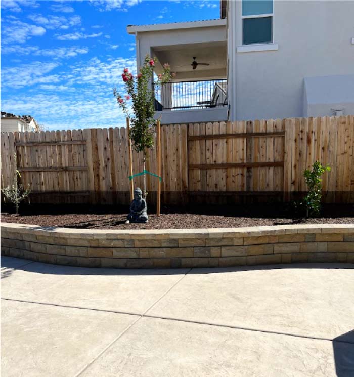 Custom curved stone retaining wall designed by a professional landscape contractor to enhance a residential tiered garden and privacy fence.
