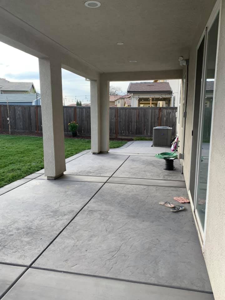 A clean, modern stamped concrete patio area under a covered porch featuring recessed lighting and a smooth, decorative gray finish.
